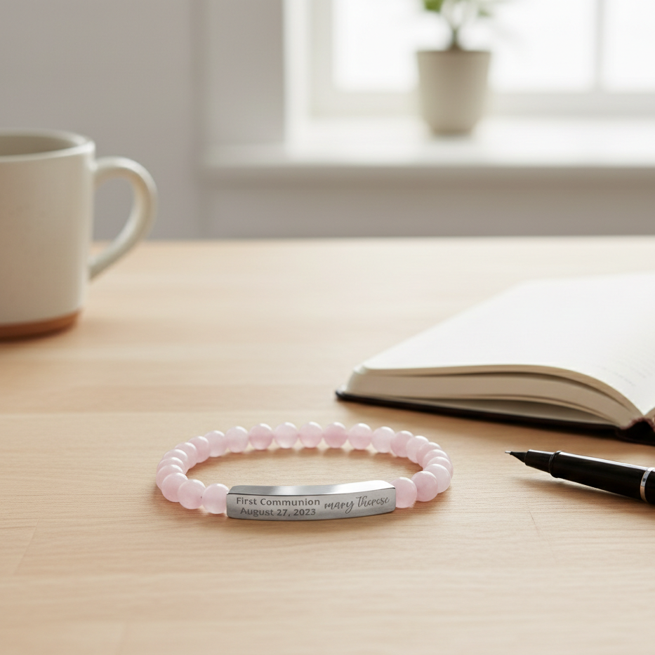 Pink beaded bracelet with engraved message on a wooden surface with a cup, notebook, and pen.