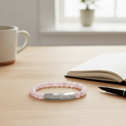 Pink beaded bracelet with engraved message on a wooden surface with a cup, notebook, and pen.